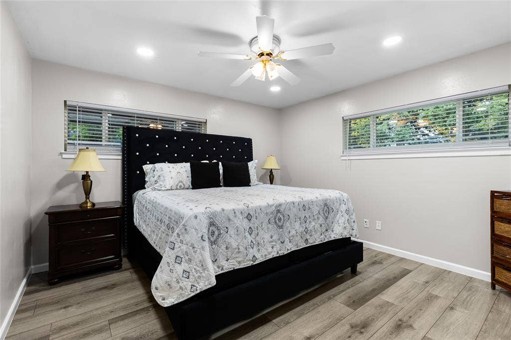Spacious room featuring wood-finish flooring, two large windows with blinds, recessed lighting, and a ceiling fan with integrated lighting