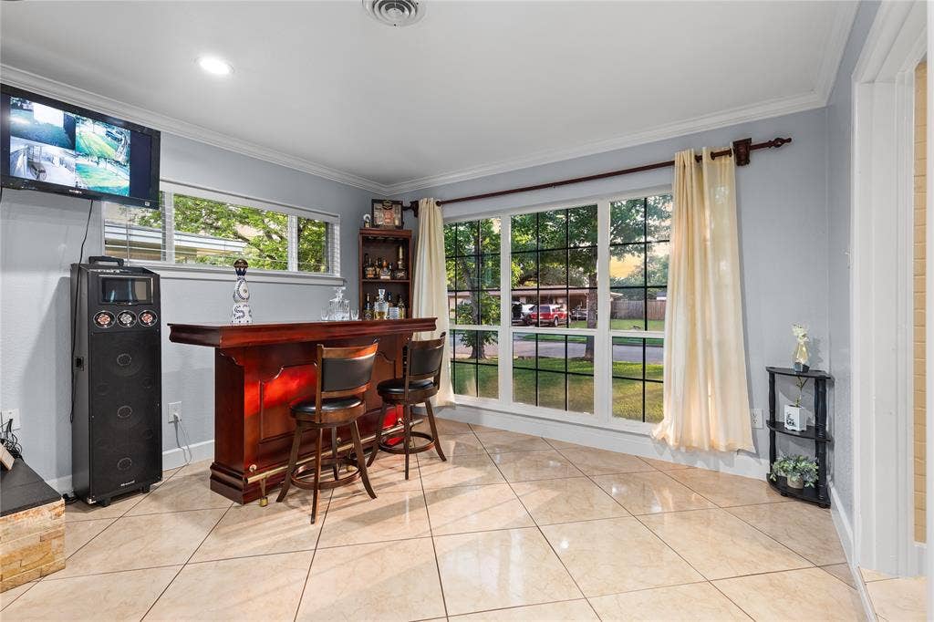 Spacious room featuring a rich wood-finish bar with brass accents, large windows providing ample natural light, recessed lighting, and tile flooring