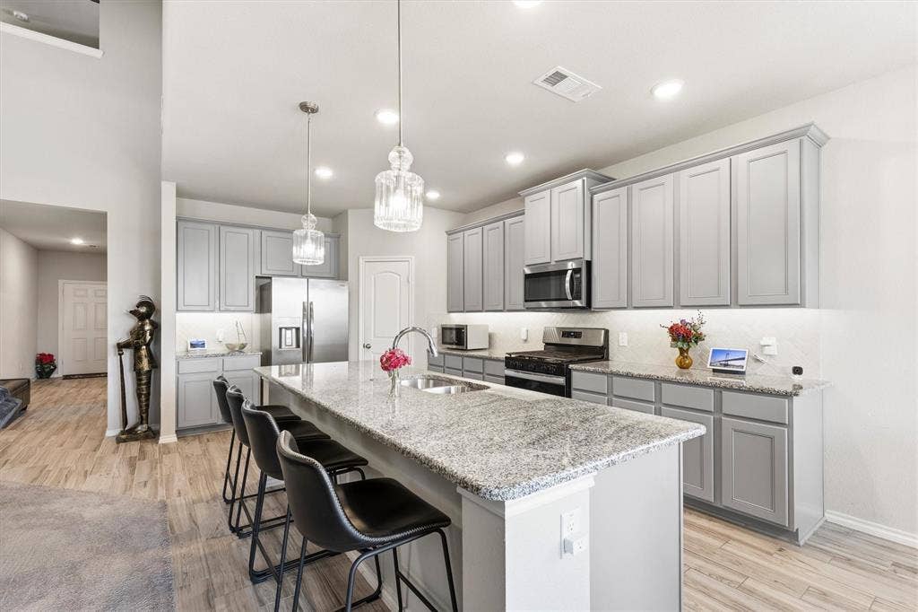 702 Matador Lane, Arlington, TX 76002 Kitchen featuring an expansive island with a double basin sink and integrated seating, light gray cabinetry, stainless steel appliances, and recessed lighting
