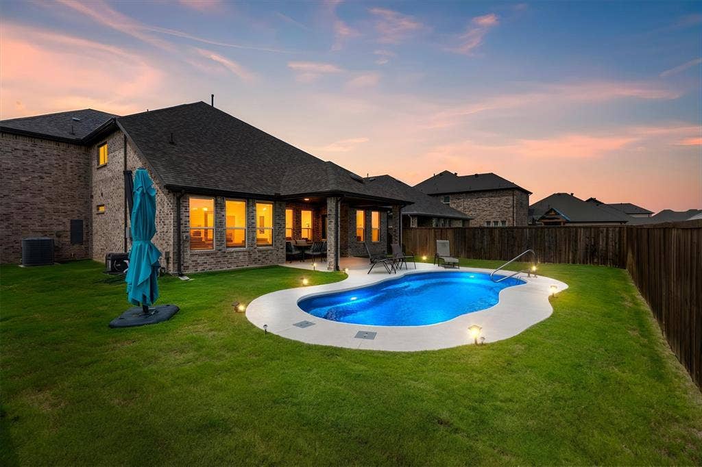 702 Matador Lane, Arlington, TX 76002 Brick exterior residence featuring a freeform swimming pool with integrated lighting, a concrete pool deck, and perimeter ground lighting