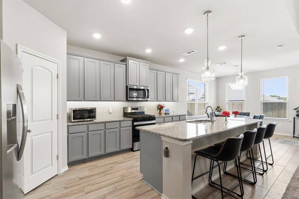 702 Matador Lane, Arlington, TX 76002 Modern kitchen featuring light gray cabinetry, wood-finish flooring, a large island with a composite countertop, recessed lighting, and pendant fixtures