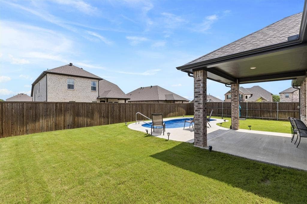 702 Matador Lane, Arlington, TX 76002 Private backyard featuring a fenced perimeter, a curved swimming pool, and a covered patio area with brick columns