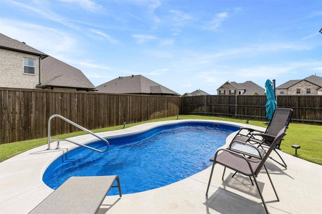 702 Matador Lane, Arlington, TX 76002 Private backyard featuring a curved inground swimming pool with a concrete surround, metal handrail, and perimeter landscape lighting