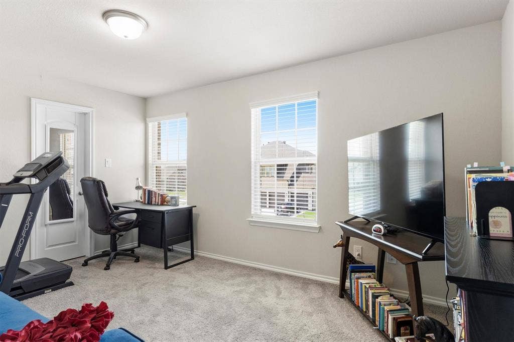 702 Matador Lane, Arlington, TX 76002 Carpeted room featuring two windows with white blinds, a white paneled door, light gray walls, and a flush mount ceiling light fixture