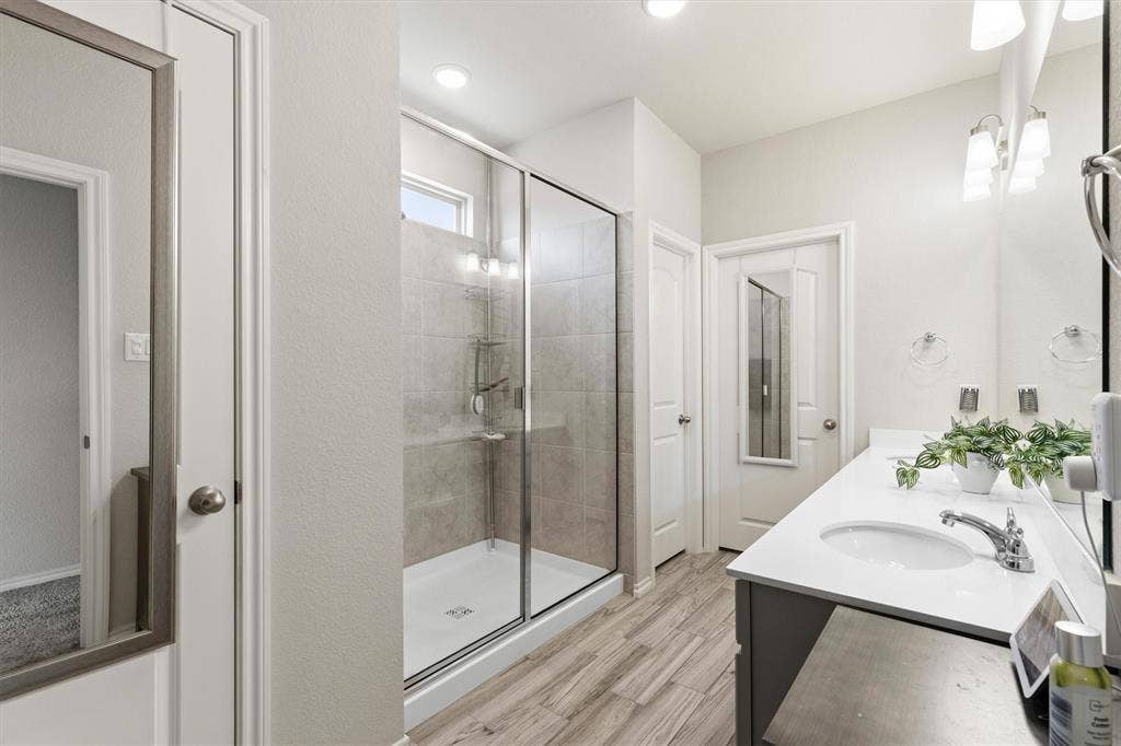 702 Matador Lane, Arlington, TX 76002 Bathroom featuring a frameless glass shower enclosure, wood-finish flooring, a double vanity with undermount sinks, and a quartz countertop