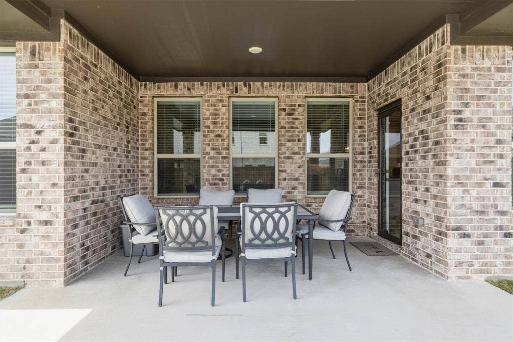 702 Matador Lane, Arlington, TX 76002 Covered concrete patio featuring a brick exterior, multiple windows with blinds, a recessed light, and an exterior door with a dark frame