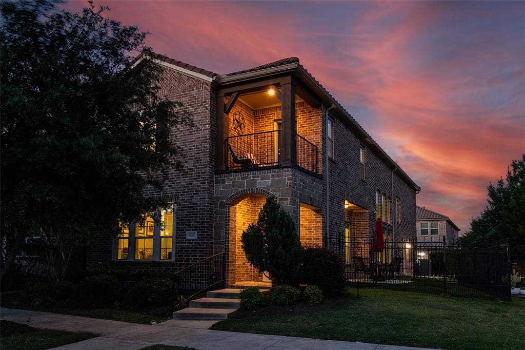 Brick and stone exterior featuring an arched entry, a second-story balcony with metal railings, and a side patio