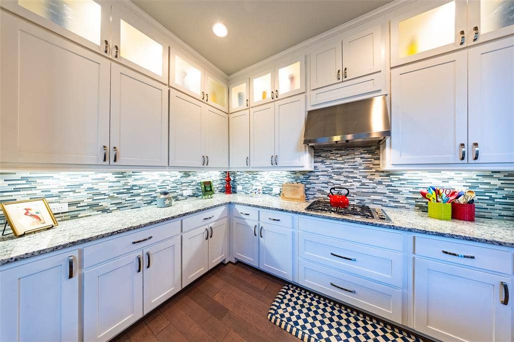 Kitchen featuring white cabinetry, granite countertops, a mosaic tile backsplash, stainless steel range hood, and wood-finish flooring
