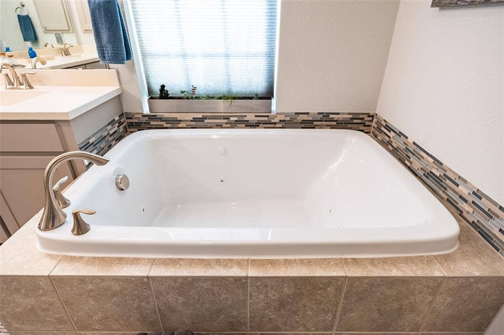 Soaking jacuzzi tub with brushed nickel fixtures, surrounded by a mosaic tile accent and large format ceramic tile