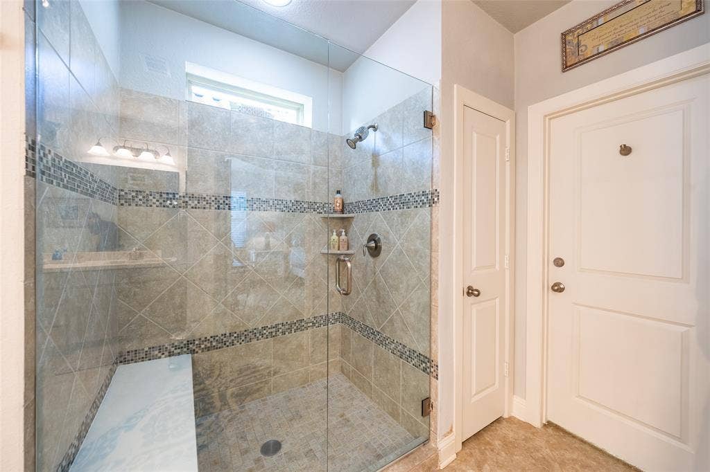 Glass-enclosed shower featuring tiled walls with decorative mosaic accents and a built-in shower bench