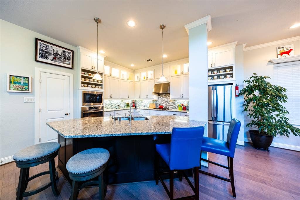 Kitchen featuring a peninsula island with granite countertop, white cabinetry with under-cabinet lighting, stainless steel appliances, a tile backsplash, and wood flooring