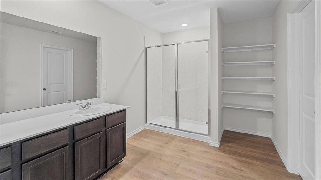 1953 Freeman Street, Tyler, TX 75704 Bathroom featuring a spacious vanity with dark wood-finish cabinetry and a white countertop, a large built-in mirror, a glass-enclosed shower, and wood-finish flooring