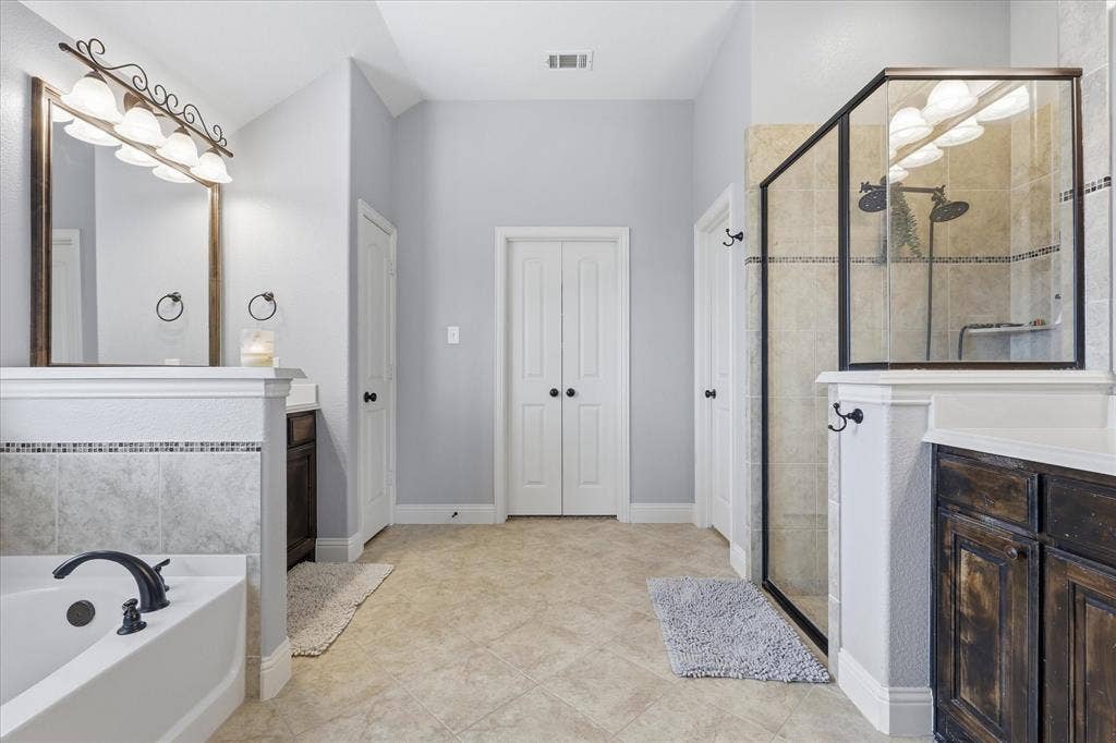 Bathroom featuring a glass-enclosed shower with dual shower heads, a separate soaking tub with dark bronze fixtures, and two distinct vanity areas with wood cabinetry and light countertops