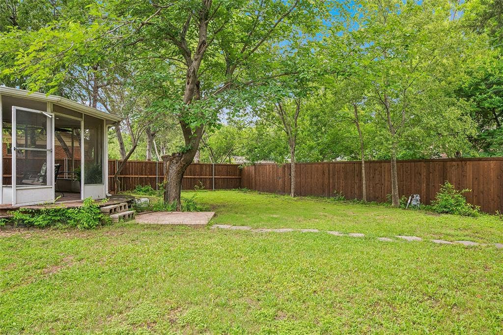 13430 Challaburton Drive, Farmers Branch, TX 75234 Expansive lawn area featuring a large mature tree, wood privacy fencing, and an enclosed screened porch with multiple entry points