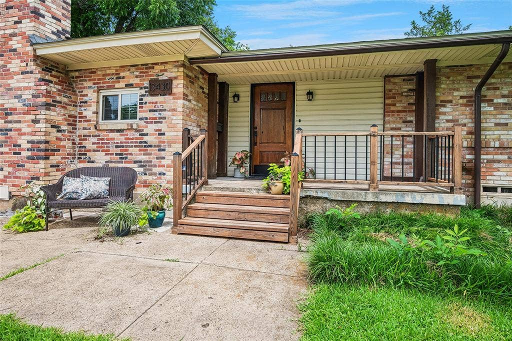 13430 Challaburton Drive, Farmers Branch, TX 75234 Inviting front porch accented with stained hardwood door. Brick and siding exterior featuring a covered porch with wood steps and railing, a solid wood entry door, and an exterior light fixture