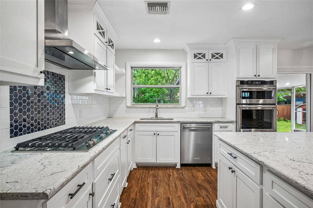 13430 Challaburton Drive, Farmers Branch, TX 75234 Open-concept kitchen featuring an island with a light-toned countertop, white cabinetry with dark hardware, built-in stainless steel appliances, and wood-finish flooring