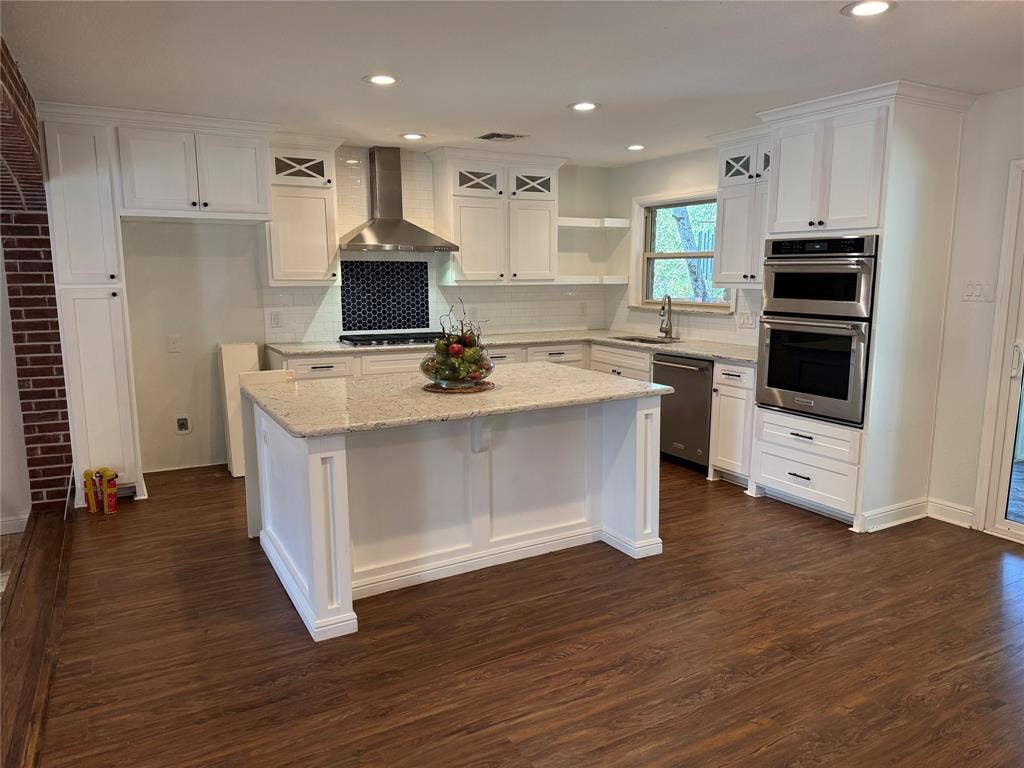 13430 Challaburton Drive, Farmers Branch, TX 75234 Spacious kitchen featuring an island with a light-toned countertop, white cabinetry with dark hardware, stainless steel appliances, and wood-finish flooring
