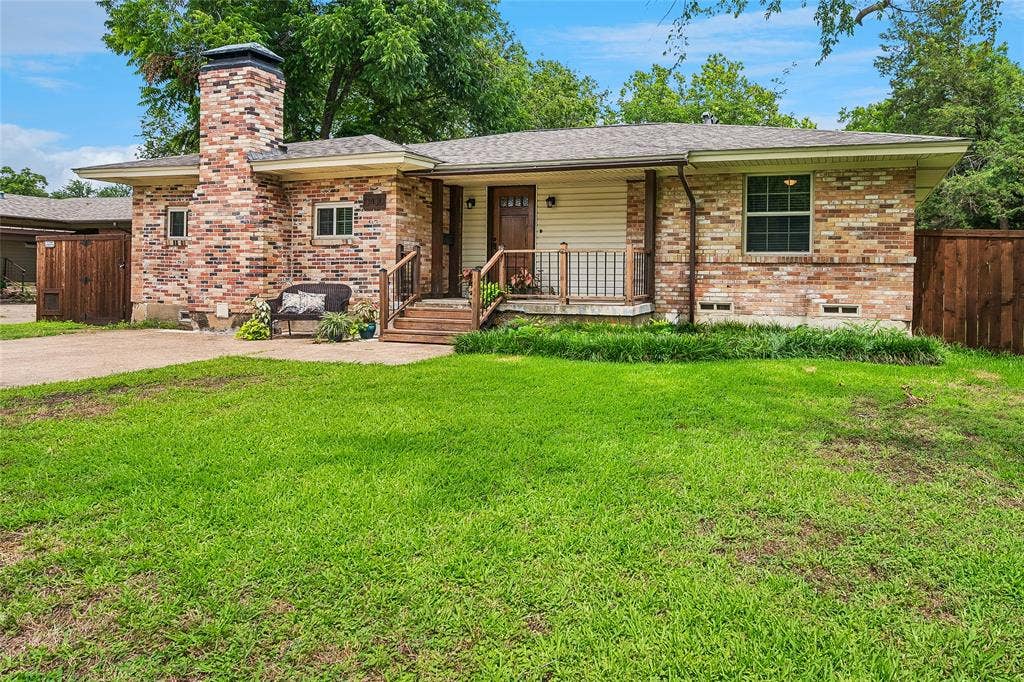 13430 Challaburton Drive, Farmers Branch, TX 75234 Brick-clad exterior with a prominent chimney, inviting front porch, and a well-kept lawn