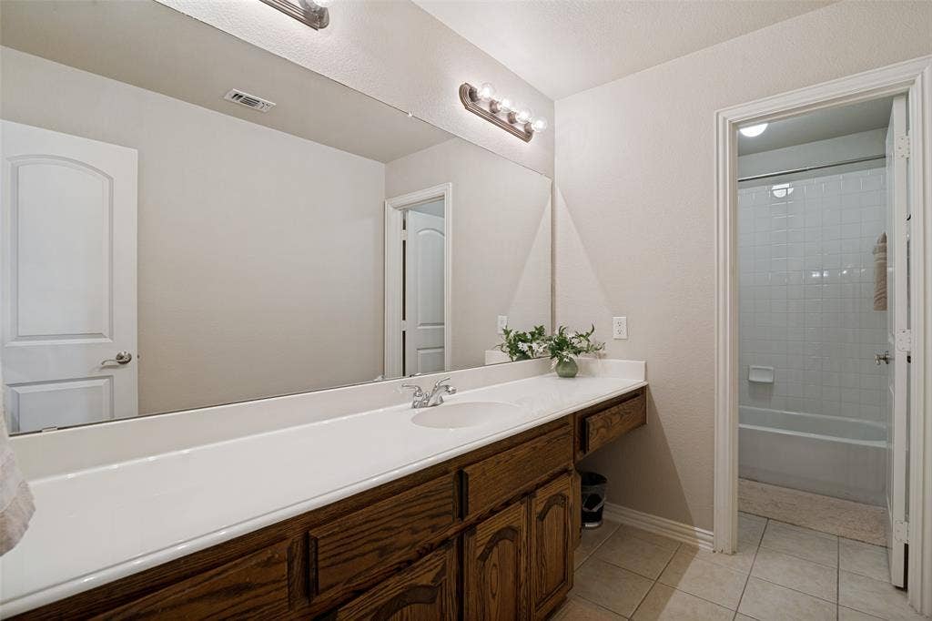 4305 Loch Haven Court, McKinney, TX 75072 Spacious bathroom featuring a long wood-finish vanity with a single basin, a large wall-mounted mirror, and tile flooring