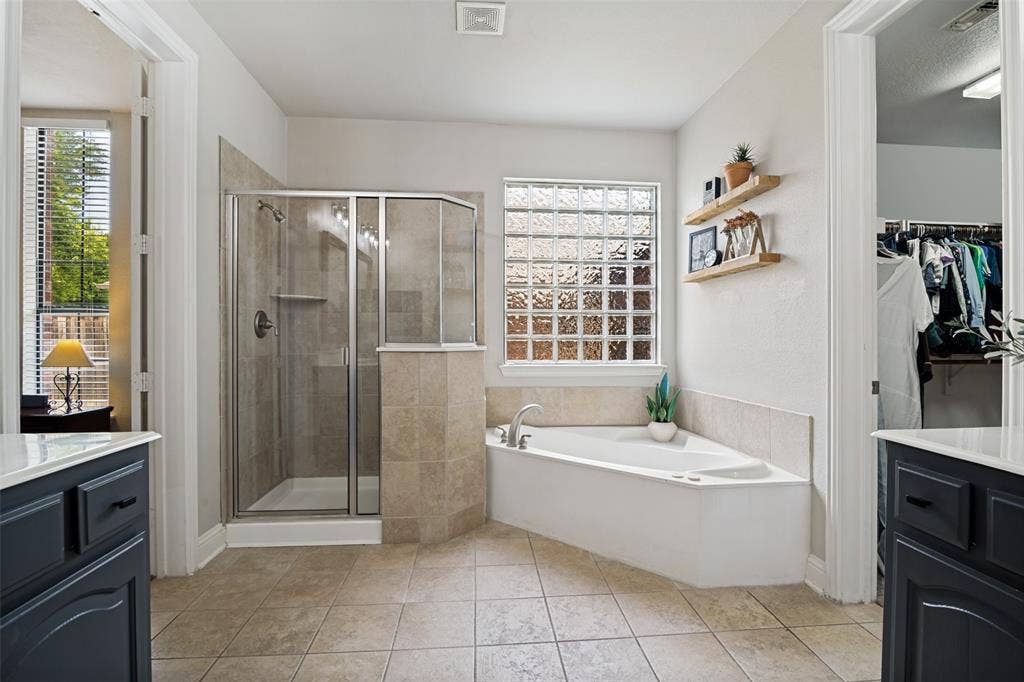 4305 Loch Haven Court, McKinney, TX 75072 Bathroom featuring a corner soaking tub, a glass-enclosed shower, and a glass block window