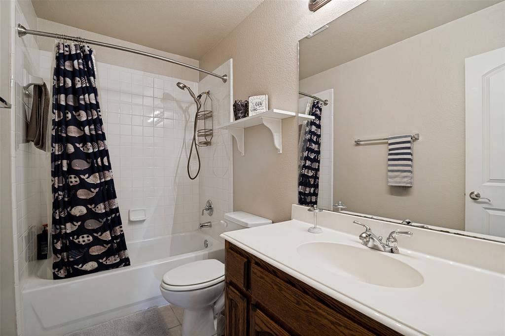 4305 Loch Haven Court, McKinney, TX 75072 Full bathroom featuring a white tub-shower combination with subway tile surround, a dark wood-finish vanity with a white integrated sink, a large wall-mounted mirror, and neutral wall paint