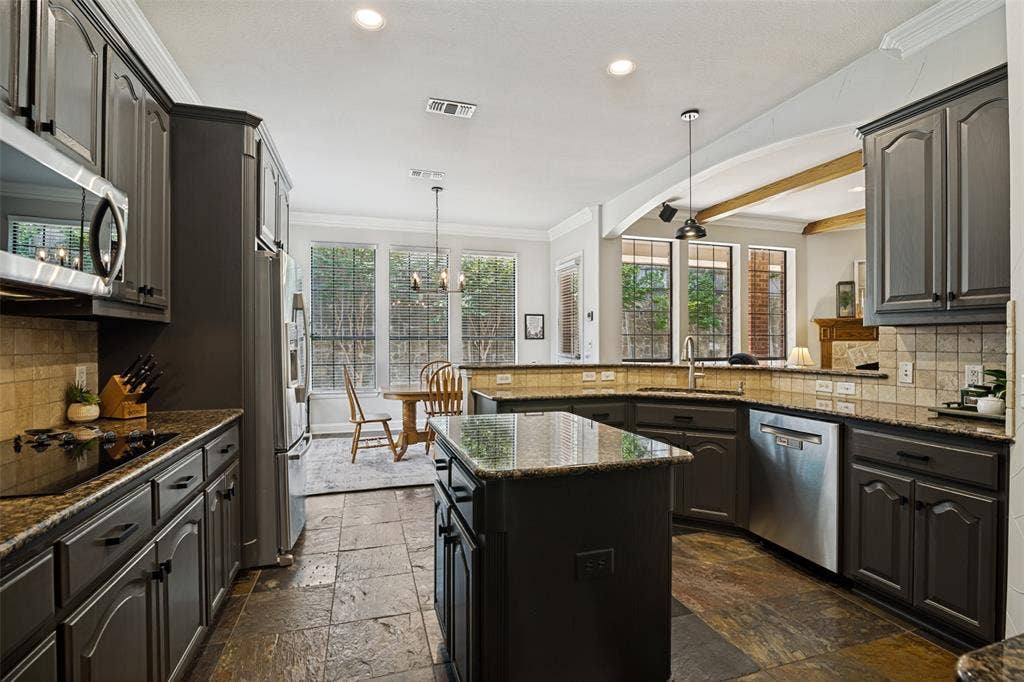 4305 Loch Haven Court, McKinney, TX 75072 Kitchen featuring dark cabinetry, granite countertops, stainless steel appliances, a central island, and stone tile flooring