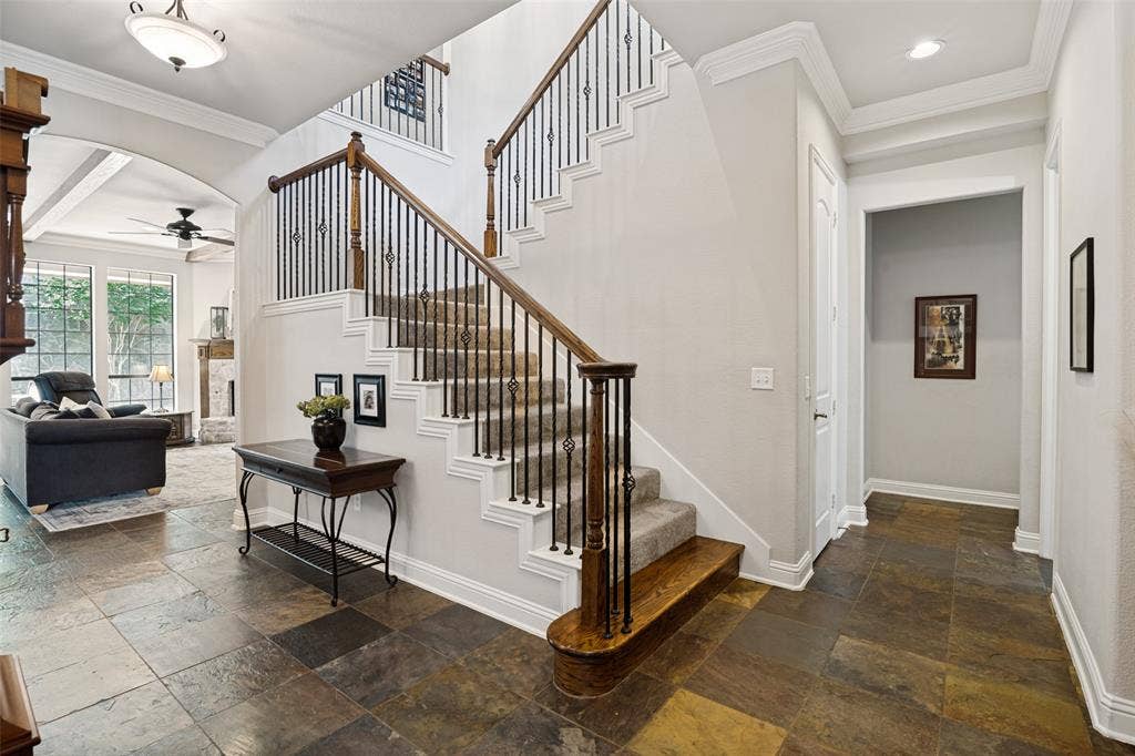 4305 Loch Haven Court, McKinney, TX 75072 Grand entryway featuring variegated slate flooring, an elegant staircase with wrought iron balusters and wood handrails, a coffered ceiling with crown molding, and a spacious archway opening to a living area with large windows