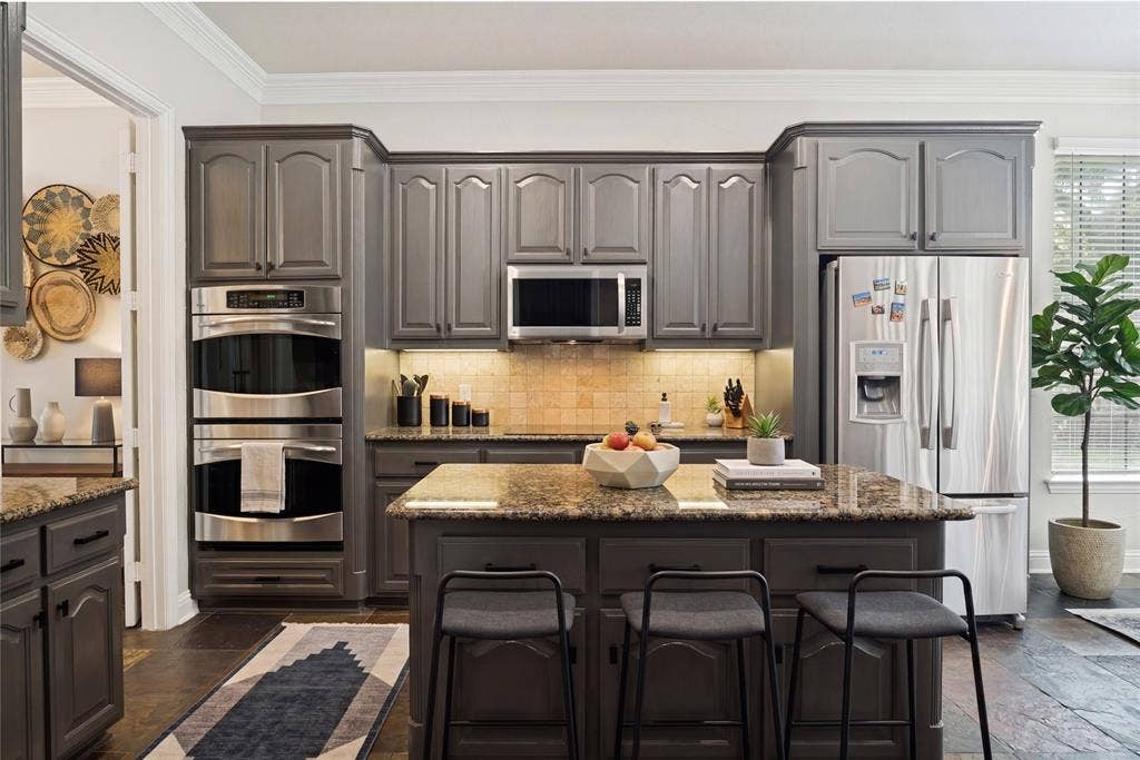 4305 Loch Haven Court, McKinney, TX 75072 Kitchen featuring dark cabinetry, stainless steel appliances, a built-in double oven, a kitchen island with seating, and stone countertops