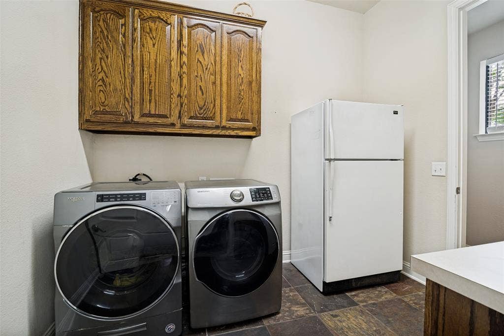 4305 Loch Haven Court, McKinney, TX 75072 Roomy laundry area featuring upper wood cabinetry, a white refrigerator, and variegated brown floor tiling