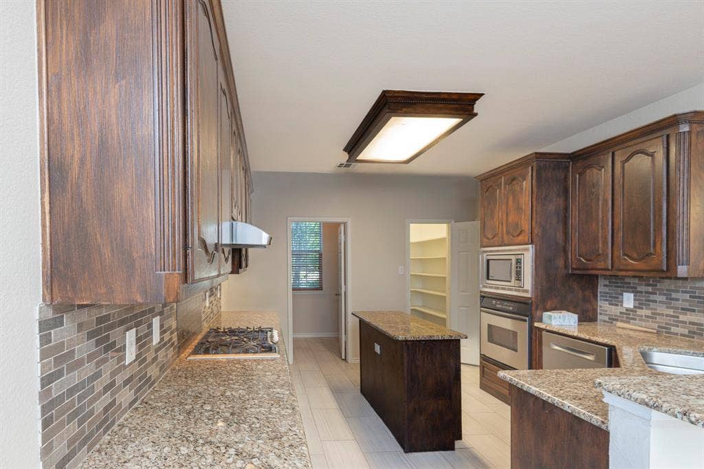 1200 Talley Lane, Frisco, TX 75033 Kitchen featuring stainless steel appliances, light stone counters, dark brown cabinetry, tasteful backsplash, and light tile flooring
