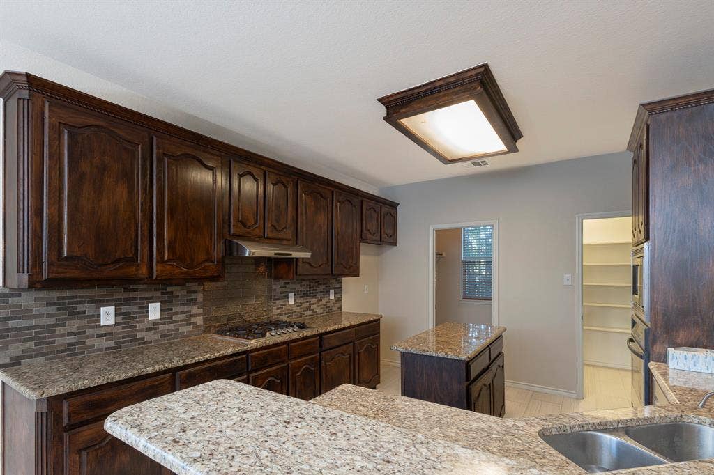 1200 Talley Lane, Frisco, TX 75033 Kitchen with light stone countertops, dark brown cabinetry, a kitchen island, backsplash, and light tile floors