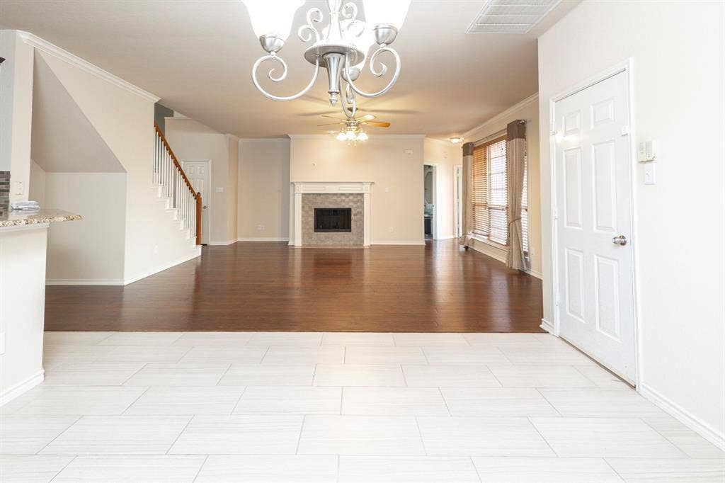 1200 Talley Lane, Frisco, TX 75033 Unfurnished living room featuring crown molding, a tiled fireplace, light tile floors, and ceiling fan with notable chandelier