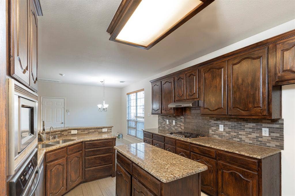 1200 Talley Lane, Frisco, TX 75033 Kitchen featuring light stone countertops, decorative light fixtures, dark brown cabinetry, sink, and light tile floors