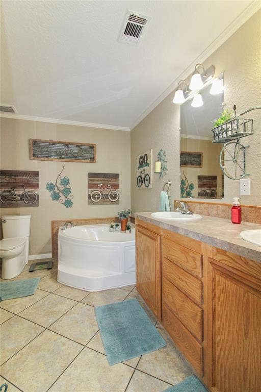 455 Hughes Cemetery Road, Italy, TX 76651 Bathroom featuring a corner soaking tub with deck-mounted fixtures, dual vanity with wood-finish cabinetry, ceramic tile flooring, and a standard toilet