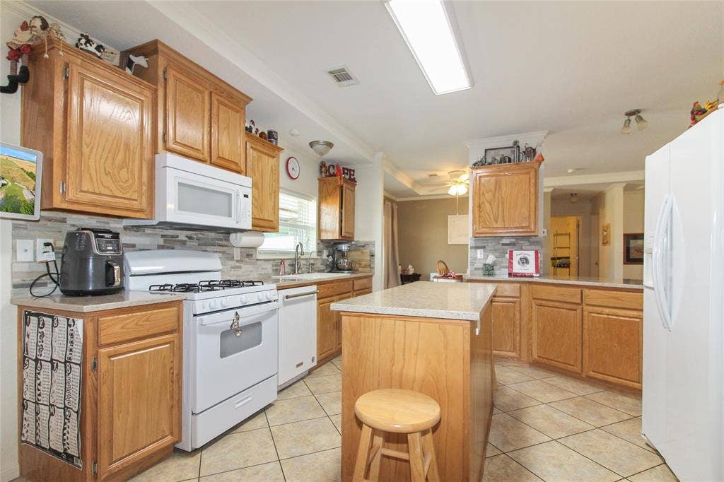 455 Hughes Cemetery Road, Italy, TX 76651 Kitchen featuring light wood-finish cabinetry, light-toned stone-finish countertops, a tile backsplash, white appliances, and tile flooring