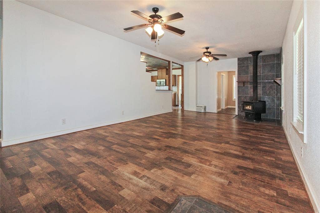 455 Hughes Cemetery Road, Italy, TX 76651 1936 HOUSE Spacious living area featuring wood-finish flooring, a freestanding wood-burning stove with a tiled surround, and multiple ceiling fans with integrated lighting
