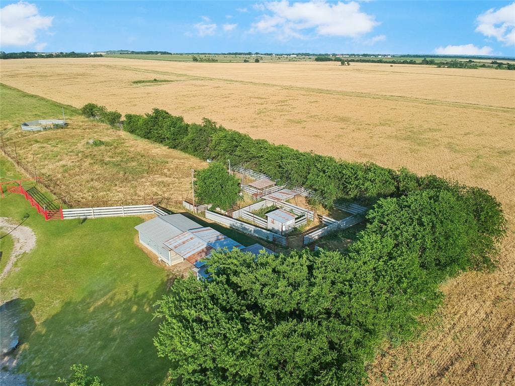 455 Hughes Cemetery Road, Italy, TX 76651 Expansive agricultural property featuring multiple fenced areas, a metal-roofed outbuilding, mature trees, and open fields