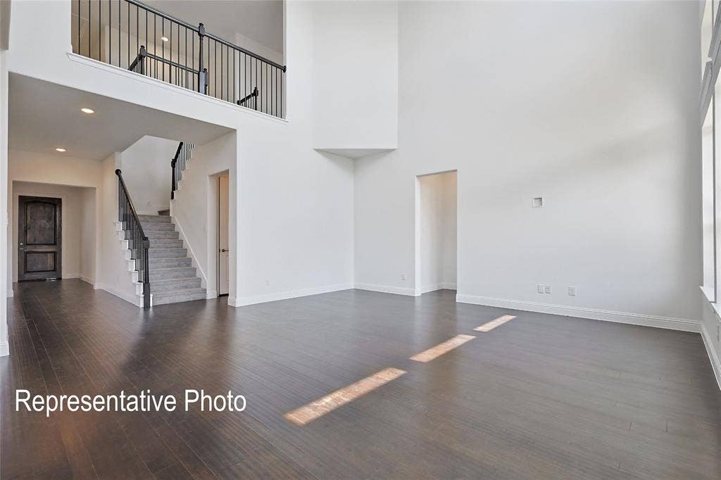 Vaulted living space featuring wood-finish flooring, a grand staircase with dark metal railings, an upper-level balcony, recessed lighting, and expansive windows