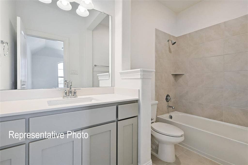 Light-toned bathroom featuring a single vanity with a white countertop and chrome faucet, a large frameless mirror, and a bathtub with tile surround