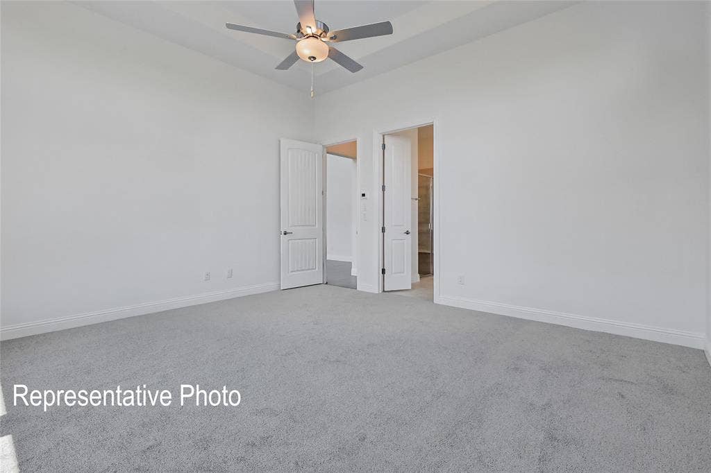 Spacious room with light gray carpeting, crisp white walls, a tray ceiling, and a ceiling fan with integrated lighting
