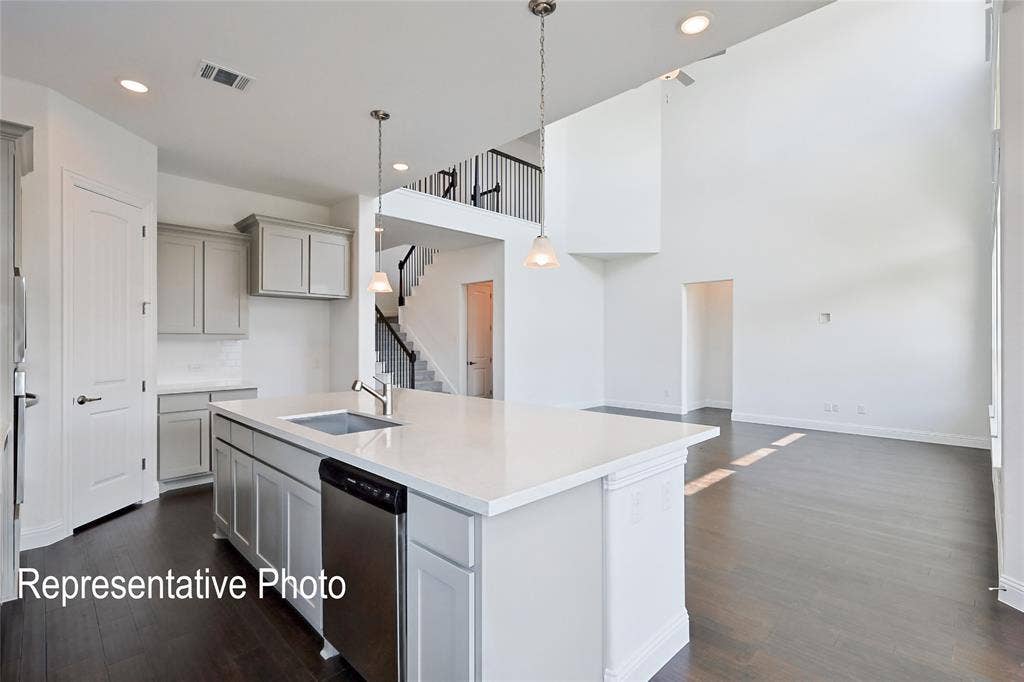 Open-concept living space featuring a spacious kitchen island with integrated sink, stainless steel dishwasher, light gray cabinetry, and high ceilings