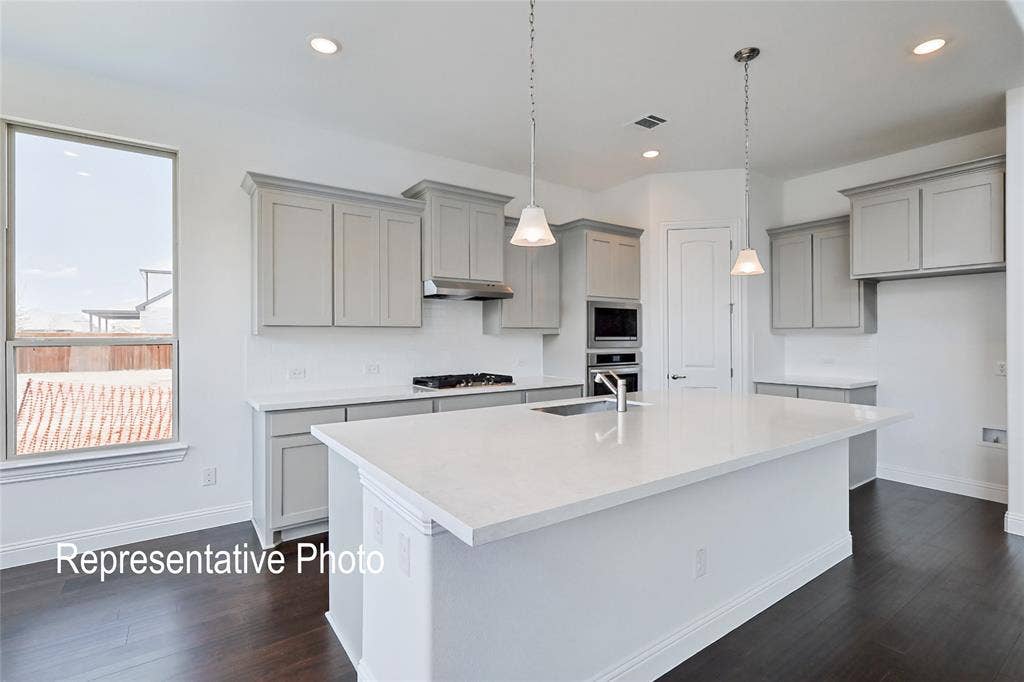 Spacious kitchen featuring an expansive island with a stainless steel sink, light gray cabinetry, white quartz countertops, white subway tile backsplash, and dark wood-finish flooring