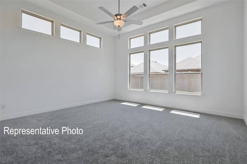 Spacious room featuring gray carpeting, white walls, multiple large windows, a ceiling fan with integrated lighting, and a high ceiling