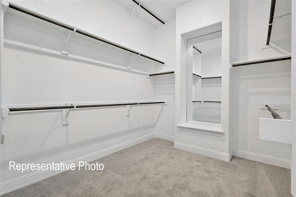 Spacious walk-in closet featuring extensive built-in shelving, multiple hanging rods, a framed pass-through opening, and gray carpet flooring
