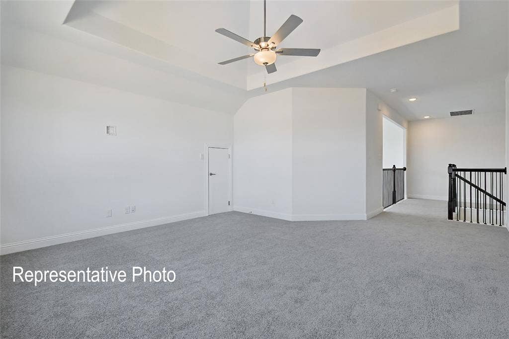 Spacious room featuring light gray carpeting, a tray ceiling, and a ceiling fan with integrated lighting