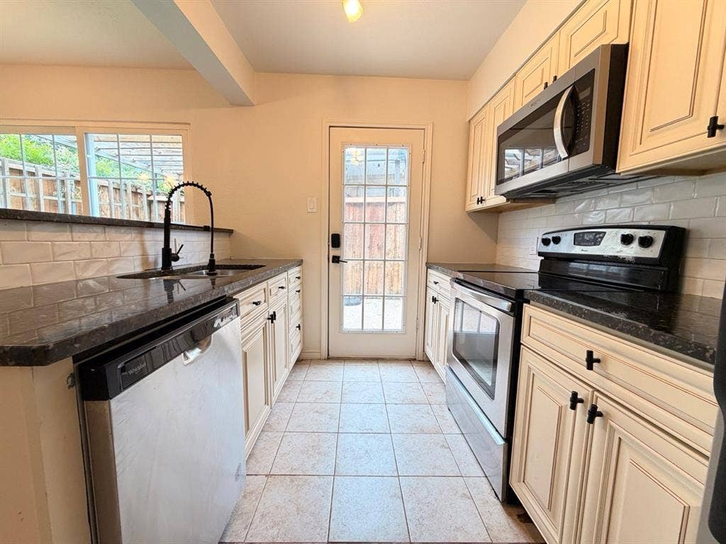 14003 Brookgreen Drive, Dallas, TX 75240 Kitchen featuring dark countertops, cream cabinetry with black hardware, and stainless steel appliances