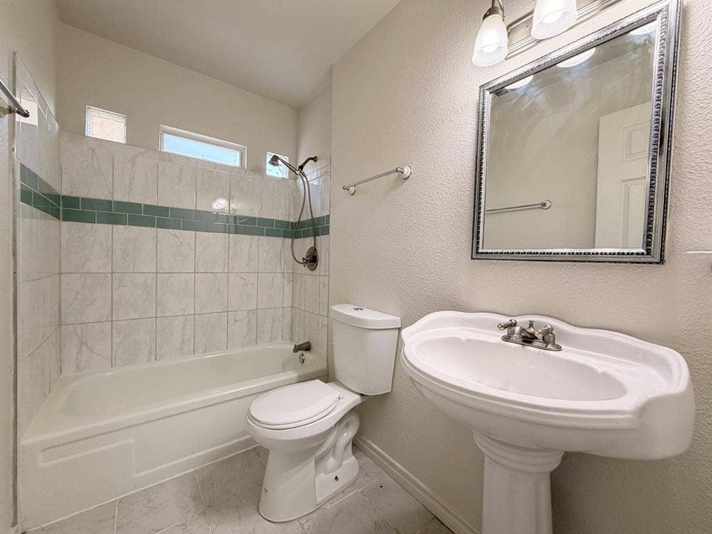 14003 Brookgreen Drive, Dallas, TX 75240 Bathroom featuring a pedestal sink, framed mirror with vanity lighting, and a bathtub with a tiled surround