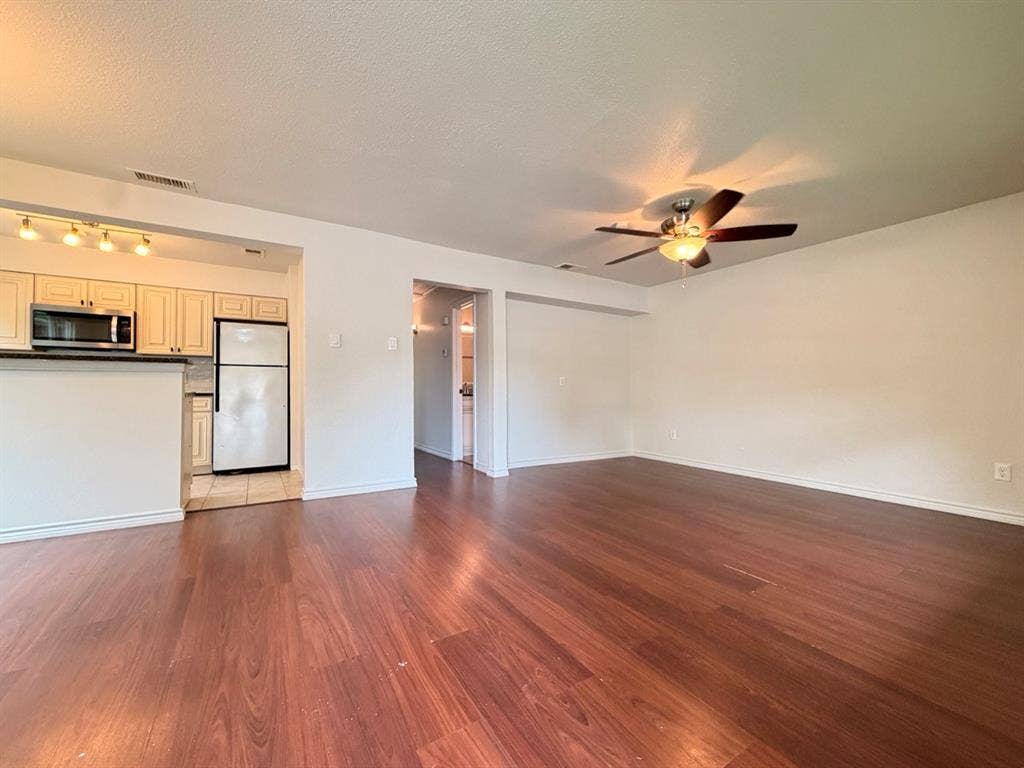 14003 Brookgreen Drive, Dallas, TX 75240 Open-concept living area featuring wood-finish flooring, a ceiling fan, and a kitchen area with track lighting, light-toned cabinetry, and dark countertops