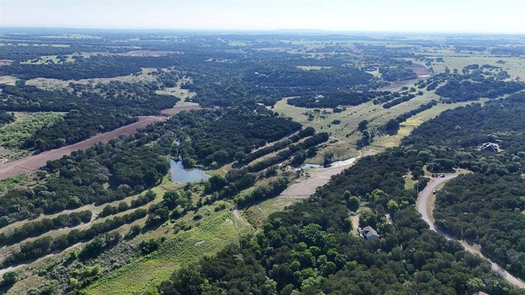 Expansive aerial landscape featuring a large body of water, extensive tree coverage, and several clearings