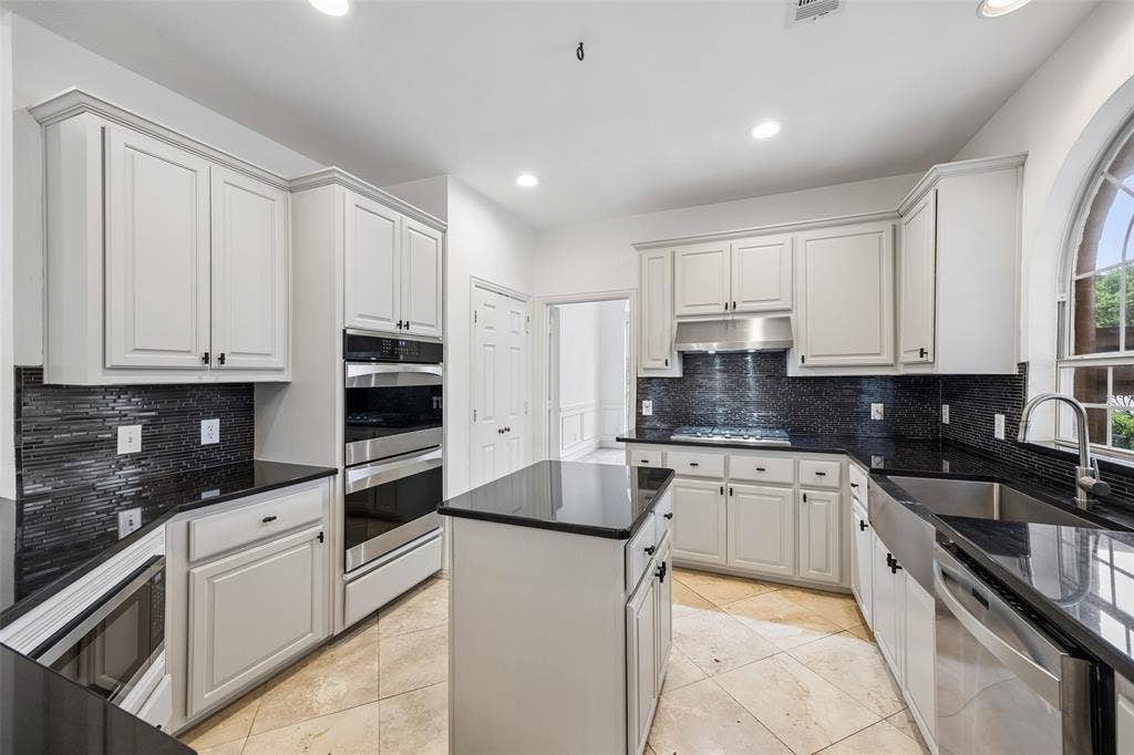 2701 Oates Drive, Plano, TX 75093 Bright kitchen featuring gray cabinetry, black countertops, a mosaic tile backsplash, stainless steel appliances, and a central island